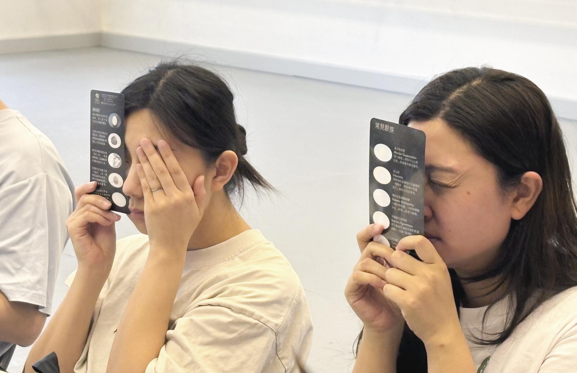 口述影像：兩名香港演藝學院的女同學，將視覺體驗卡直向緊貼眼前，她們分別閉上或以手掩蓋左眼，聚精會神地體驗視障人士的視覺世界。